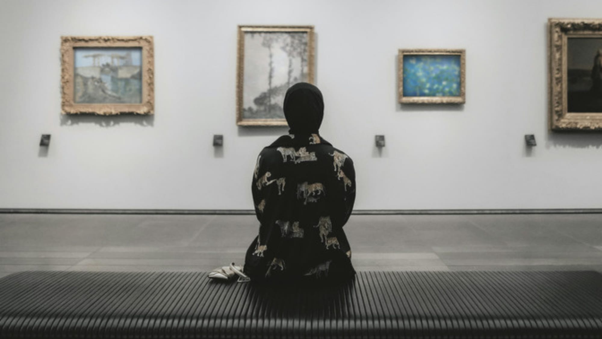 A lone person sits in a gallery looking at paintings, an editorial metaphor for attention and what anyone actually sees on a website