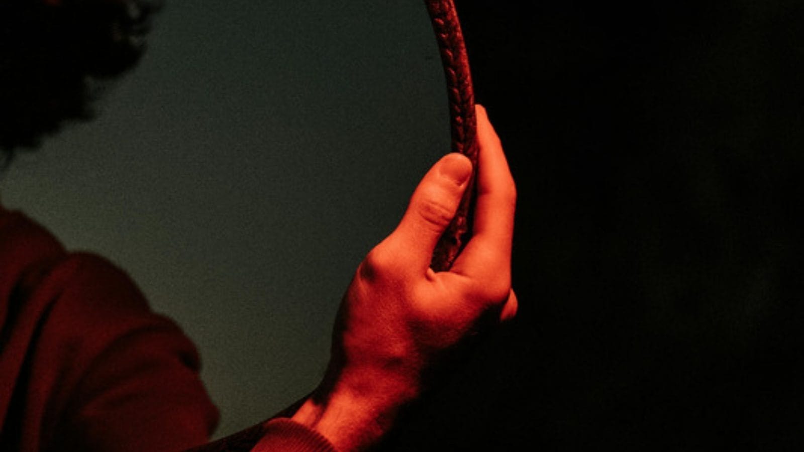 A hand holding a round mirror in dim red light