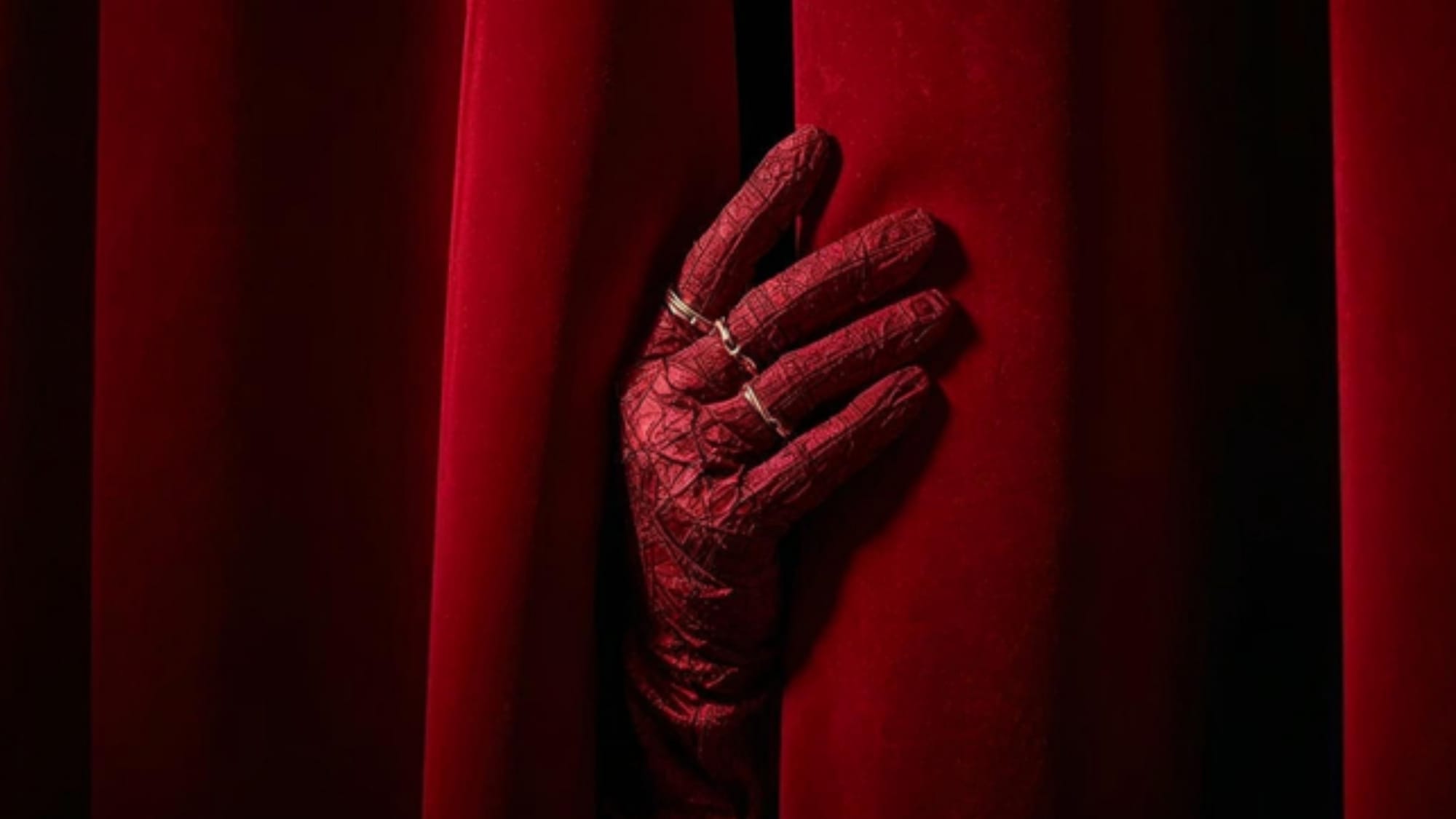 A hand in a glove by a red theatre curtain, a nod to cinemas and film premieres