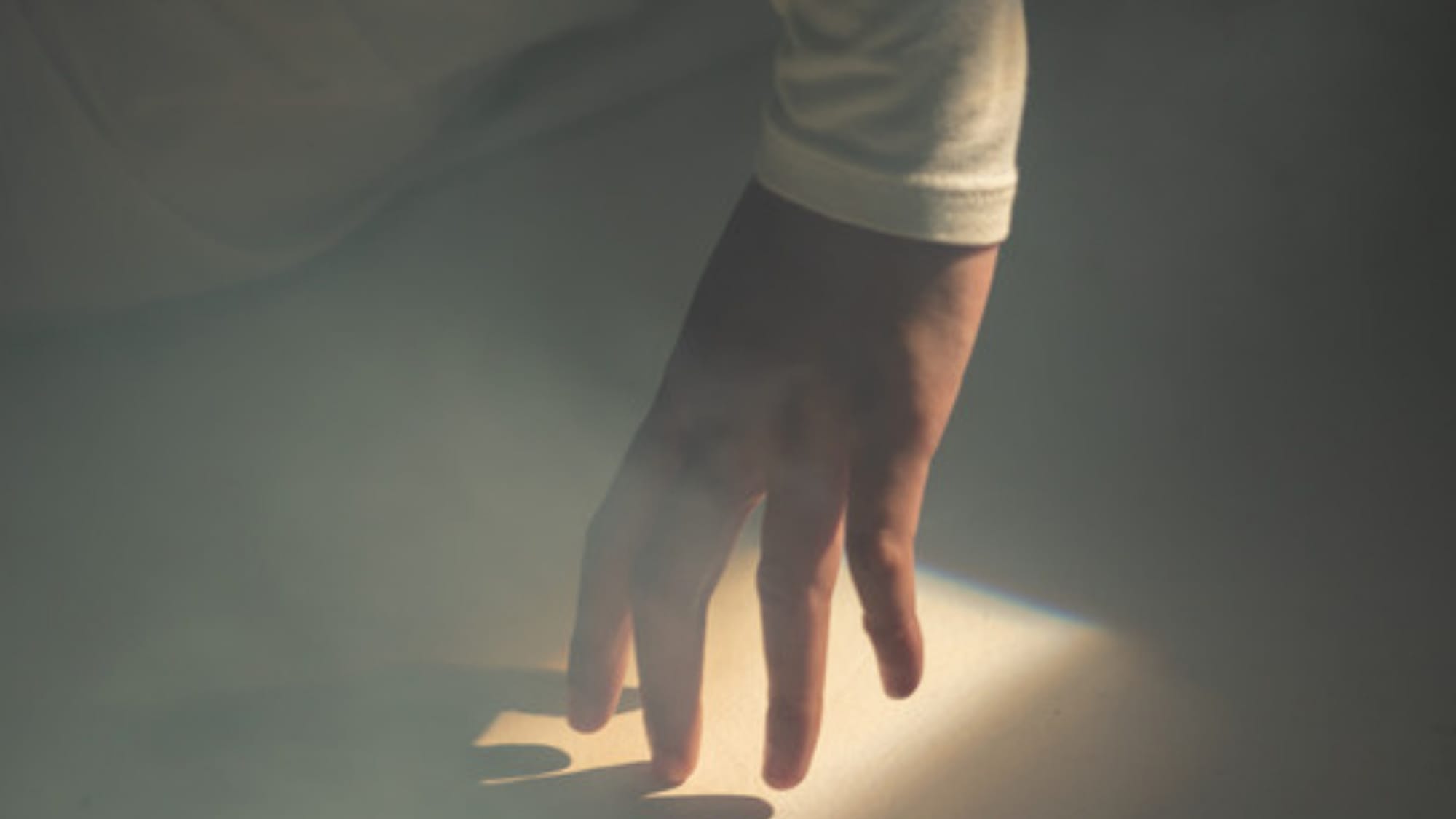 A hand reaching into a cone of light in the dark