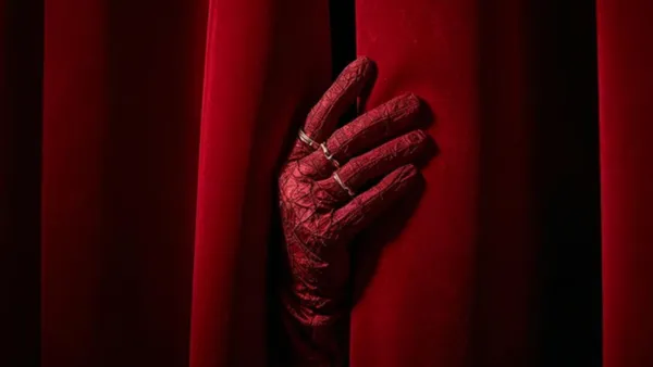 Ruka v rukavici u rudé divadelní opony jako odkaz na kina a filmové premiéry