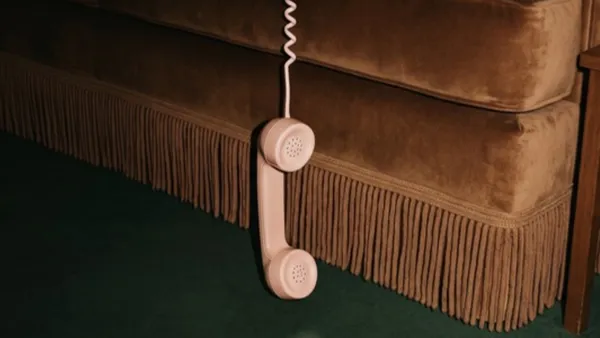 Růžové telefonní sluchátko visící na kroucené šňůře před gaučem
