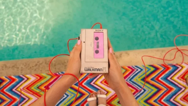 Ruce drží retro walkman s růžovou kazetou u bazénu