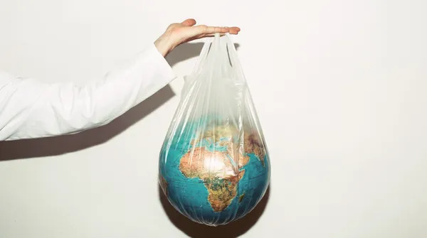 Ruka v bílém rukávu drží průhlednou igelitovou tašku, ve které je glóbus s mapou Afriky a Evropy
