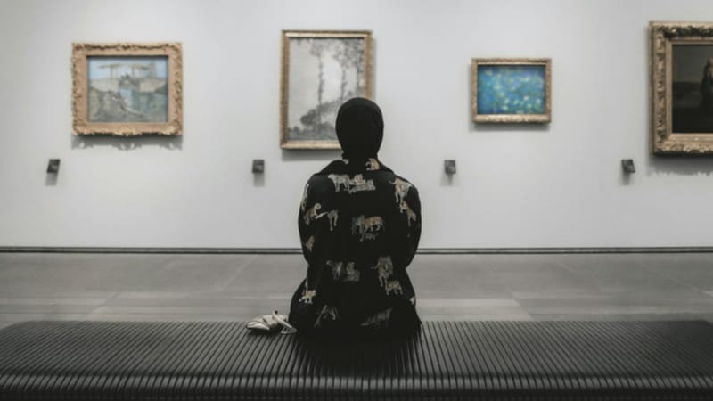 Osamělý člověk sedí v galerii a dívá se na obrazy. Editorialní metafora pozornosti a toho, co na webu někdo skutečně uvidí.