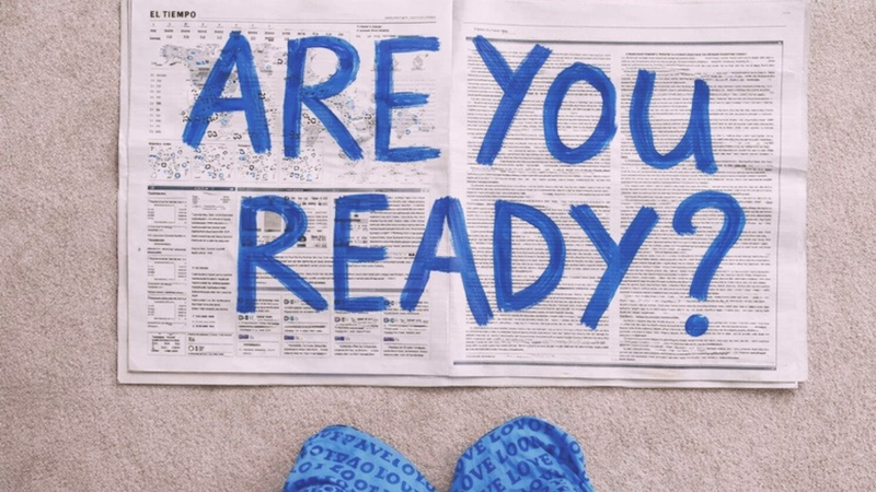 Rozevřené noviny s modrým ručně malovaným nápisem ARE YOU READY? a žabkami pod nimi