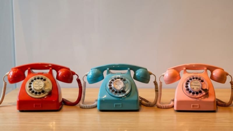 Tři retro telefony v červené, modré a růžové barvě vedle sebe na stole