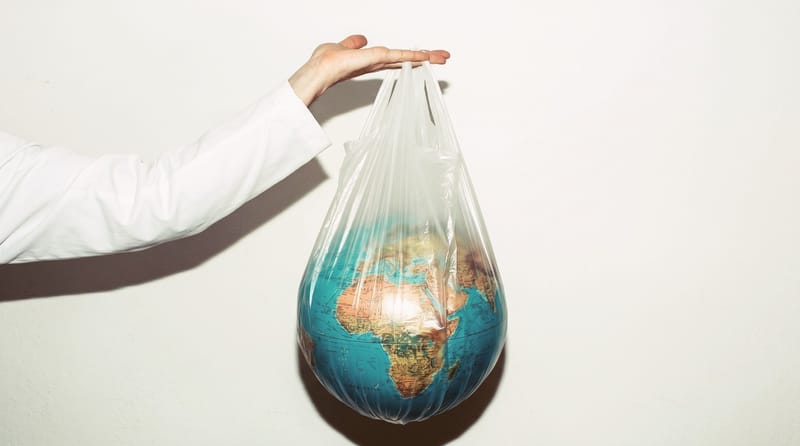 Ruka v bílém rukávu drží průhlednou igelitovou tašku, ve které je glóbus s mapou Afriky a Evropy